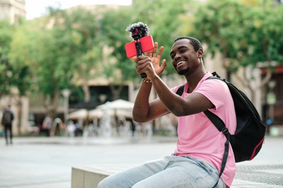 Homem sorrindo enquanto transmite com celular e microfone ao ar livre.