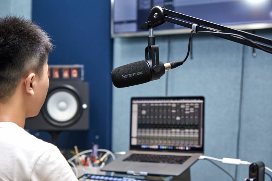 Homem gravando podcast sentado em frente a notebook com microfone de diafragma grande SR-BV1 posicionado acima da sua cabeça.