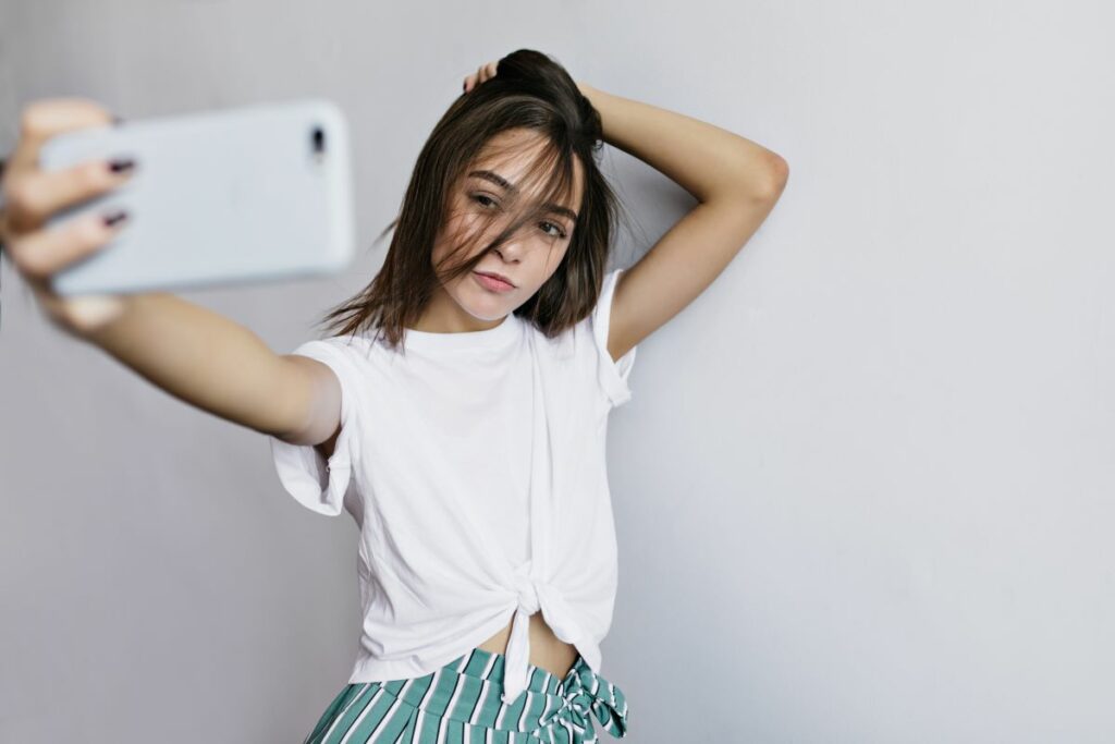 menina tocando seu cabelo enquanto tira foto dentro de si mesma usando a selfie do celular