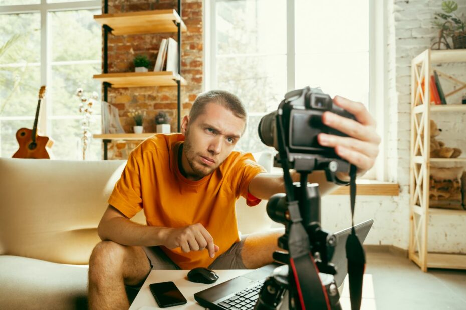 Jovem blogueiro gravando vídeos dem casa com uma câmera profissional.