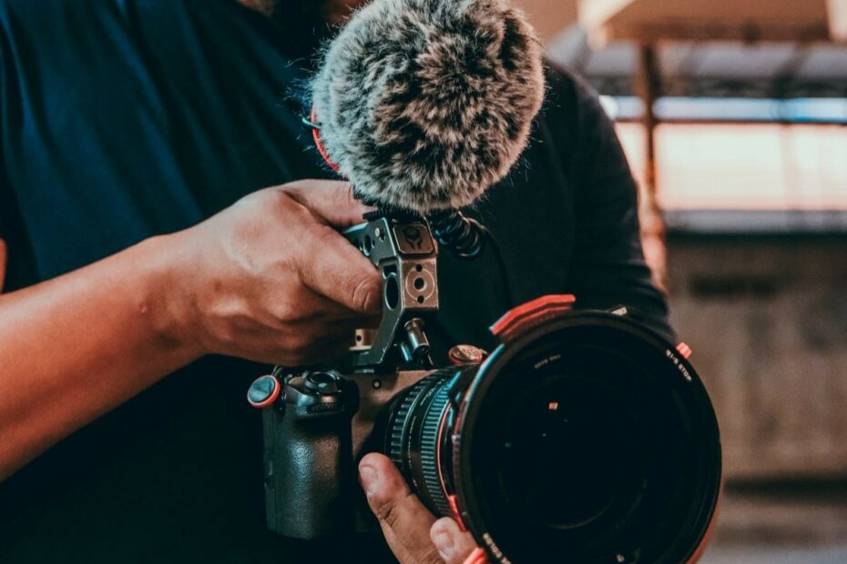 Mão direcionando câmera de filmagem com microfone direcional acoplado.