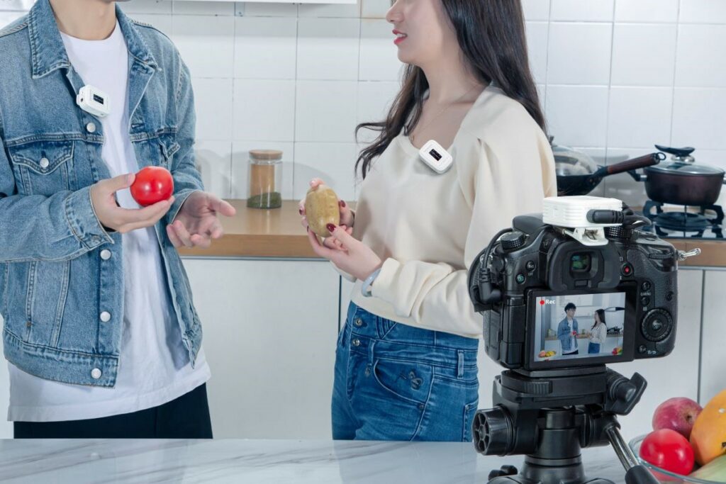 Homem e mulher posicionados em frente à câmera, utilizando um microfone de lapela da série Saramonic Blink500, enquanto conversam atrás de um balcão.